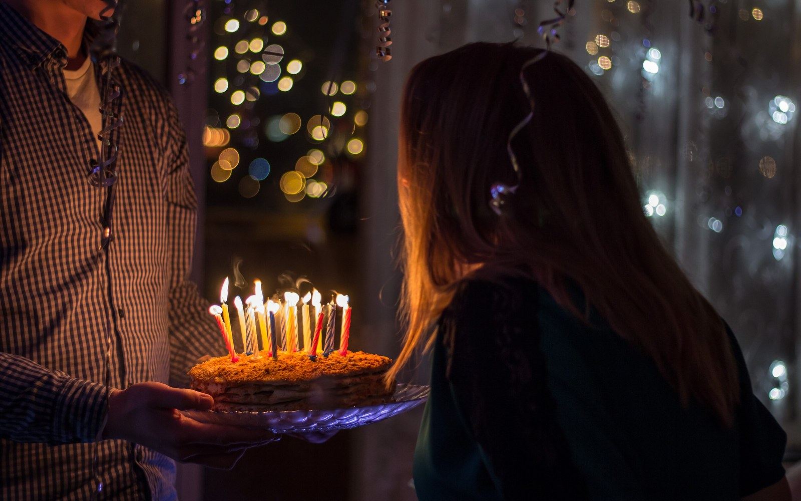 A birthday cake carried to the table, candles lit, in a darkened room